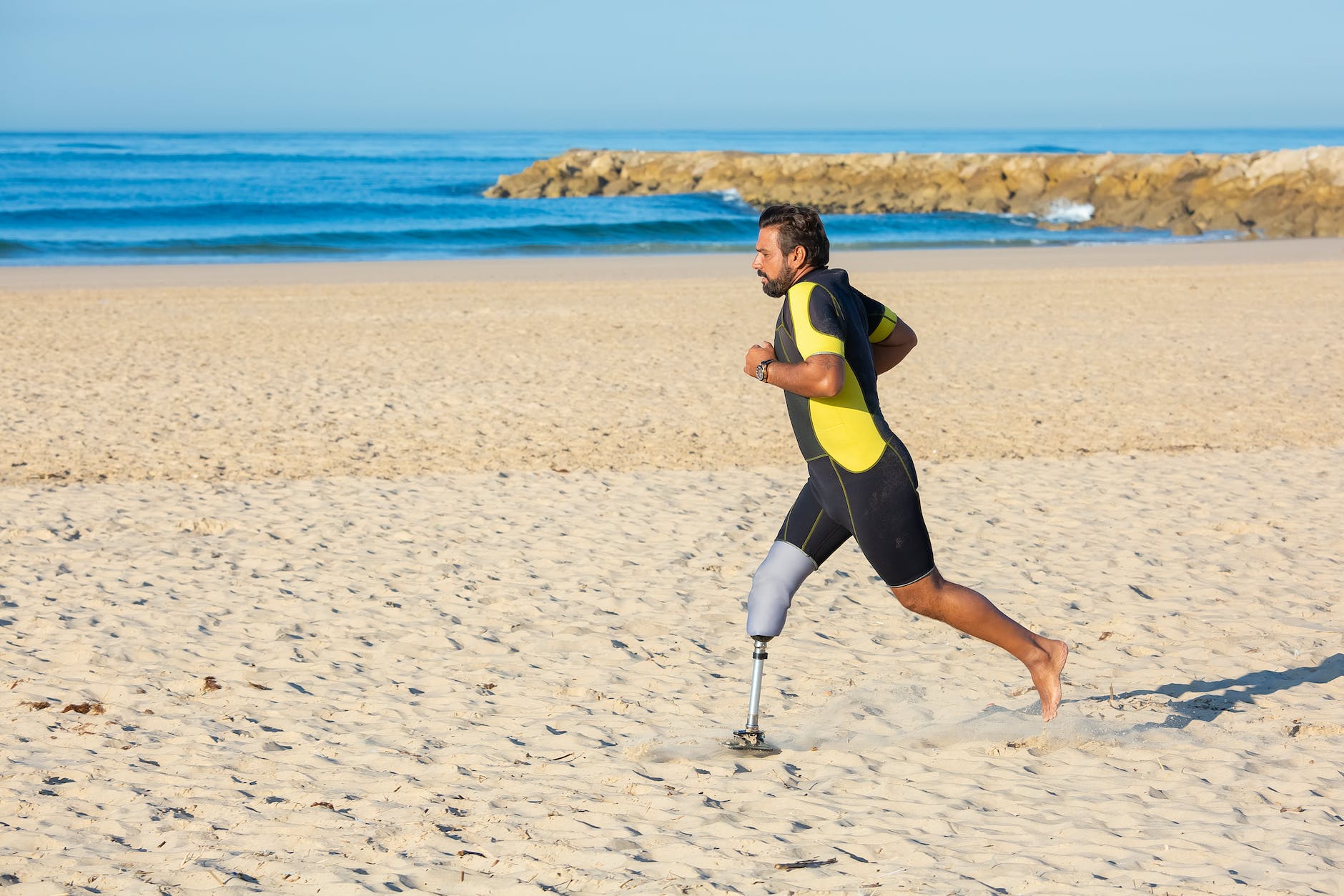 determined sportsman with leg prosthesis running on sandy coastline
